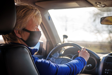 Senior woman in black protective  mask and inside a car  and lookiing at the side mirror. Right-hand drive. Coronavirus infection control concept. Pandemic coronavirus 2020