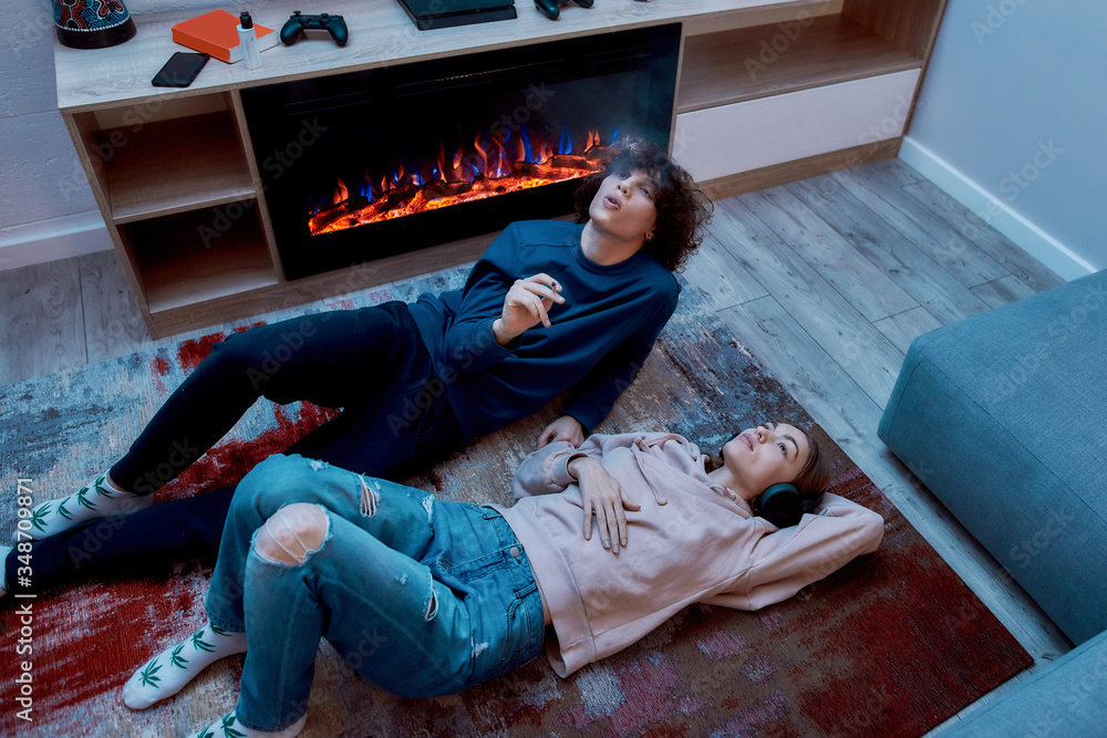Young teenage couple smoking marijuana and relaxing together while lying on  the floor at home. Guy smoking cannabis weed cigarette. Girl listening  music Stock Photo | Adobe Stock