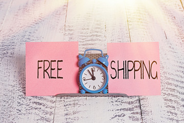 Writing note showing Free Shipping. Business concept for Freight Cargo Consignment Lading Payload Dispatch Cartage Mini blue alarm clock standing above buffer wire between two paper