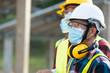 © visoot - Workers wear protective face masks for safety working in Solar cell Farm through field of solar panels,Corona virus has turned into a global emergency.