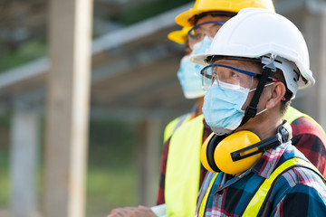 Wall Mural - Workers wear protective face masks for safety working in Solar cell Farm through field of solar panels,Corona virus has turned into a global emergency.