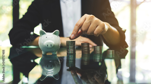 Cuadros en Lienzo Businesswoman stacking coins with a white piggy bank on the table for saving mon