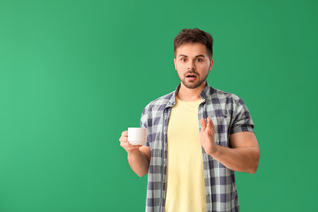 Canvas Print - Shocked man with cup of hot coffee on color background