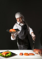 Chef cook with knife stands at the table with a plate of salmon fish