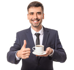 Young businessman with cup of hot coffee showing thumb-up on white background