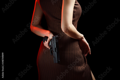 Fotografía Woman hiding handgun behind her back on black background.
