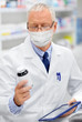 © Syda Productions - medicine, healthcare and technology concept - senior apothecary wearing face protective medical mask for protection from virus disease with tablet pc computer at pharmacy