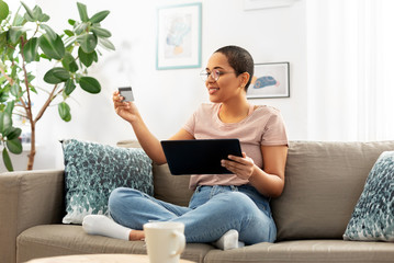 Wall Mural - internet banking, online shopping and technology concept - happy smiling african american woman sitting on sofa with tablet pc computer and credit card at home