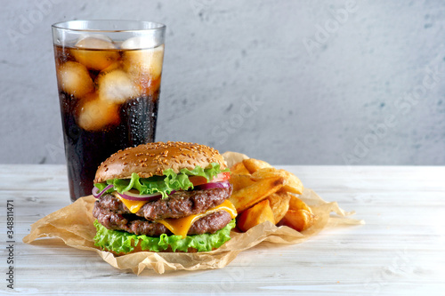 Double cheeseburger with fried potatoes and a glass of cola on a light background © Olga