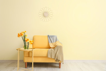 Interior of living room with stylish armchair, mirror and blooming flowers