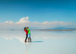 Couple in Salt Flats Uyuni Bolivia. Romantic tourists on beautiful mirror reflection on blue sky and cloud. DRONE Shot in Salar de Uyuni salt flat. Holiday, love, adventure vacation honeymoon travel
