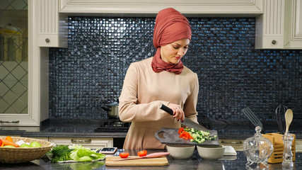 Wall Mural - attractive housewife in hijab put cut fresh vegetables in deep plates preparing halal food for husband closeup