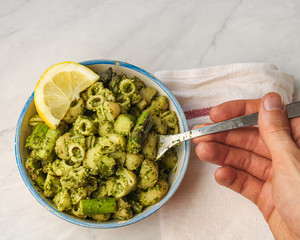 Poster - Bowl of pesto pasta with asparagus and lemon. Male hand with fork ready to eat. Top view. White background. 