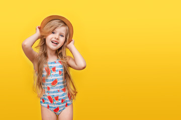 Portrait of a happy child a little blonde girl with long hair in a swimsuit and a hat on a Colored yellow background. The concept of recreation. Summer time