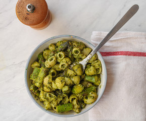 Poster - Bowl of pesto pasta with asparagus and lemon. Male hand with fork ready to eat. Top view. White background. 