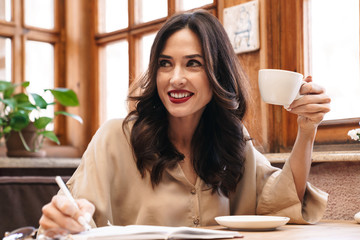 Sticker - Image of happy adult woman making notes in diary and drinking coffee