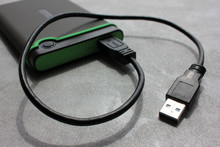 Gray And Green External Hard Drive For Backup With USB Cable On Gray Concrete Background With Copy Space.