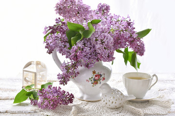 Wall Mural - purple lilac blossoms in porcelain vase and cup of coffee on white table