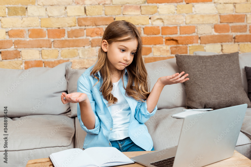 confused kid showing shrug gesture and looking at laptop - obrazy, fototapety, plakaty 