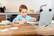 © LIGHTFIELD STUDIOS - selective focus of boy writing in notebook near laptop while e-learning at home