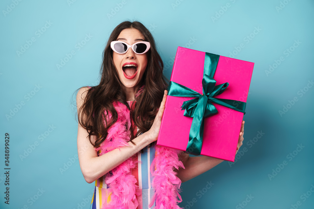 Image of surprised woman in sunglasses holding gift box - obrazy, fototapety, plakaty 