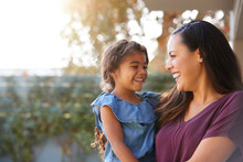 Smiling Hispanic Mother Holding Daughter Laughing In Garden At Home