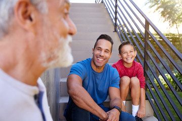 Wall Mural - Smiling Multi-Generation Male Hispanic Family Sitting On Steps In Garden And Talking Together