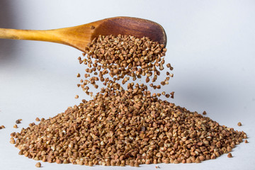 Buckwheat is poured from a wooden spoon onto a handful of buckwheat. Photo on a white background