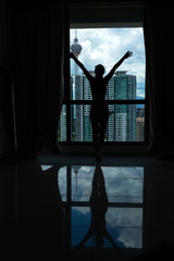 A slender girl is looking at the city through a large window. High floor.