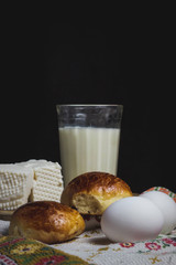 Two homemade buns with a glass of milk. Near two boiled eggs and white homemade cheese