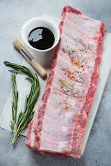 Wall Mural - Raw seasoned pork ribs with bbq sauce on a light-blue stone surface, vertical shot, selective focus