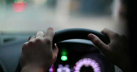 Wall Mural - Driver point of view, hands holding steering wheel driving in evening in urban city.