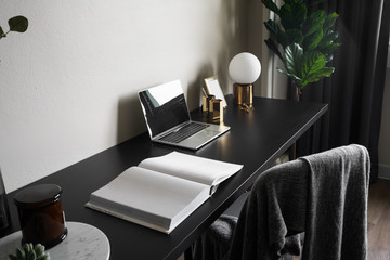 Wall Mural - Bedroom working corner decorated with laptop, white candles and artificial plant in glass vase on black wood  working table with beige painted wall in the background /apartment interior / copy space