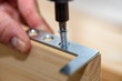 Close up on hands with cordless screwdriver assembling furniture