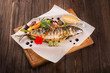 Grilled mackerel served on a wooden board with vegetables and sauce.