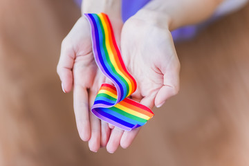 hand hold a rainbow of LGBT tapes on a LIGHT background. Copy space for text. The concept of homosexuals and LGBT people.