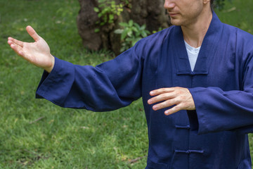 Young man practicing Qi Gong, Tai Chi or Reiki at the park wearing traditional chinese clothes. Chinese martial arts for a healthy life. Healing art. Strong handsome guy with beautiful hands.