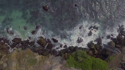 Wall Mural - Top view on a waterfall against a background of crashing waves on a rocky shore.