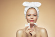 Girl in bandage on head uses beauty gua sha jade quartz roller. Satisfied smile. Perfect glowing skin, massage.