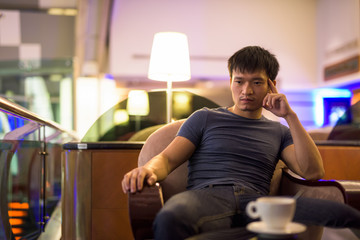 Portrait of young Asian man thinking and sitting inside the mall