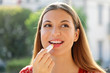 Portrait of a happy young woman applying lip balm in summer time outdoor
