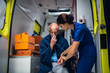 © Anna Kosolapova - Man sitting with an oxygen mask in an ambulance, woman in a medical uniform is checking his pulse