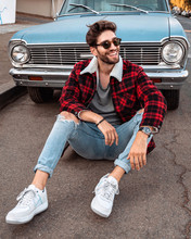 Handsome Man Wearing Plaid Red Jacket And Sunglasses, Sitting On The Street, In Front Of Vintage Car.
