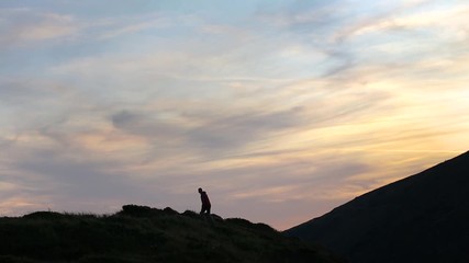 Sticker - Dark silhouette of a hiker climbing a mountain at sunset reaching summit like a winner.