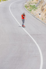 Wall Mural - Male caucasian longboarder riding downhill on an empty road, preparing for a speed tuck on the next turn he has to make. Wearing a red t-shirt green hat and black jeans.