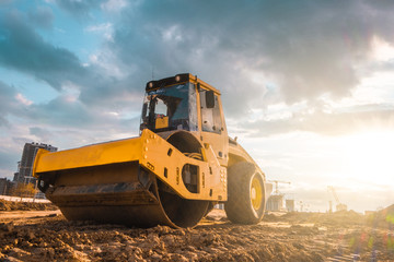 Beautiful sunset above the road roller working on the new road construction site