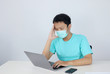 © Reezky - Young Asian man wearing medical mask is feeling unhealthy, tired, and confused with working in laptops on the table.