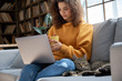 © insta_photos - Young hispanic latin ethnic teen girl relaxing sit on comfortable sofa with cute pet cat watching remote education webinar class, movie series on laptop drinking warm tea in cozy sunny living room.