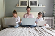 © natalialeb - Mom and Three children sitting on bed with laptops