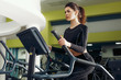 © Artyom - Young brunette girl, in black training leggings and long sleeve top engaged on treadmill in the gym. Free space for text, concept of fitness club